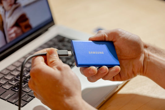 A person holding a blue device in front of a laptop