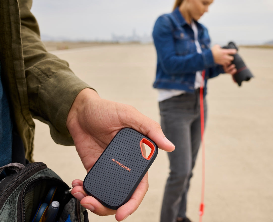 A hand holds a portable ssd, another person uses camera.