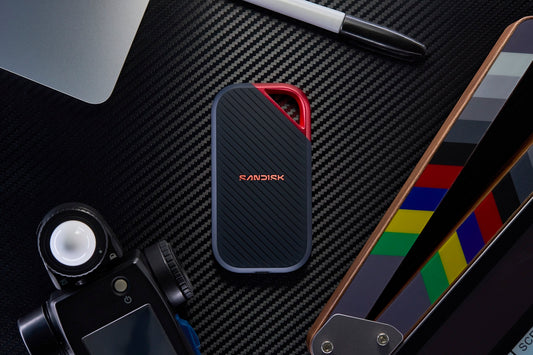 Portable ssd, camera, clapperboard, and laptop on a dark surface.